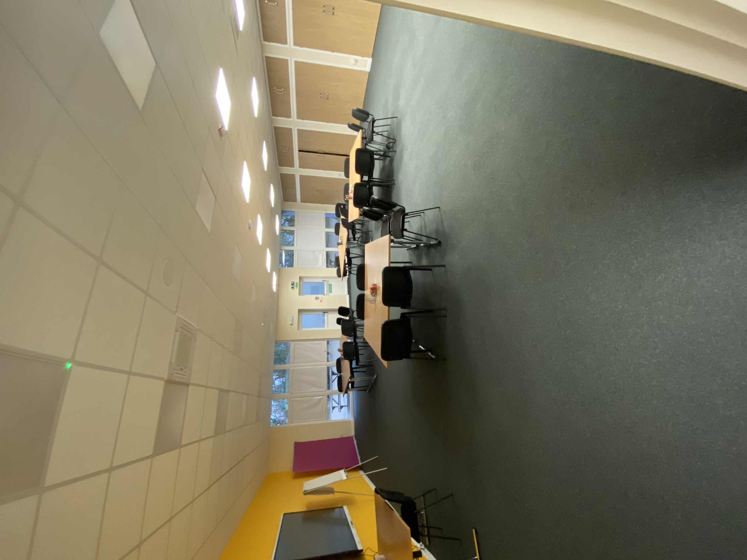 Empty classroom with tables, chairs, and large windows.