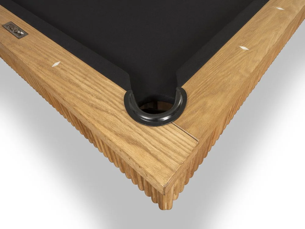 Close-up of a pool table corner with wooden edges and a black cue ball pocket.