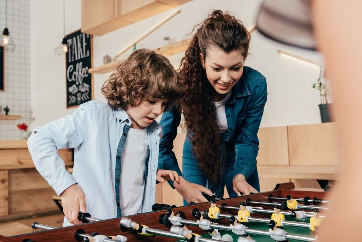 A boy and a woman playing foosball together in a cafe-style setting.