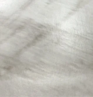Close-up of a light-colored, possibly fabric surface with faint wrinkles or creases.