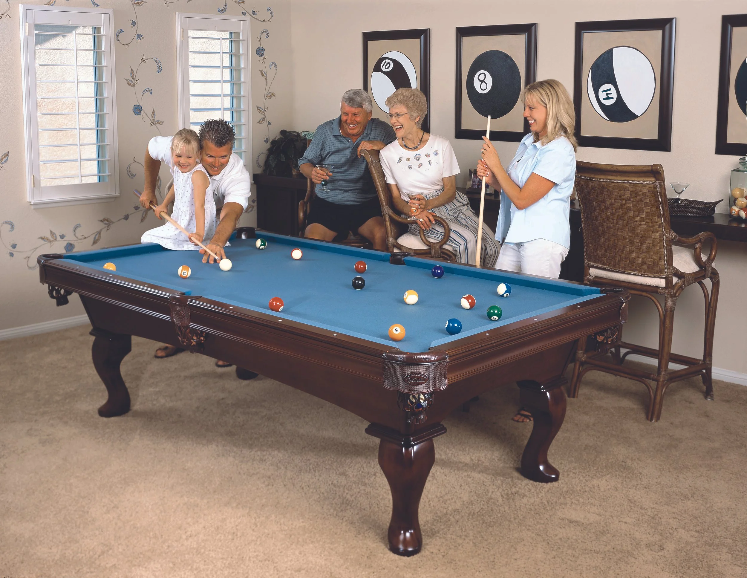 Family playing pool in a living room, with framed billiard-themed artwork on the wall.