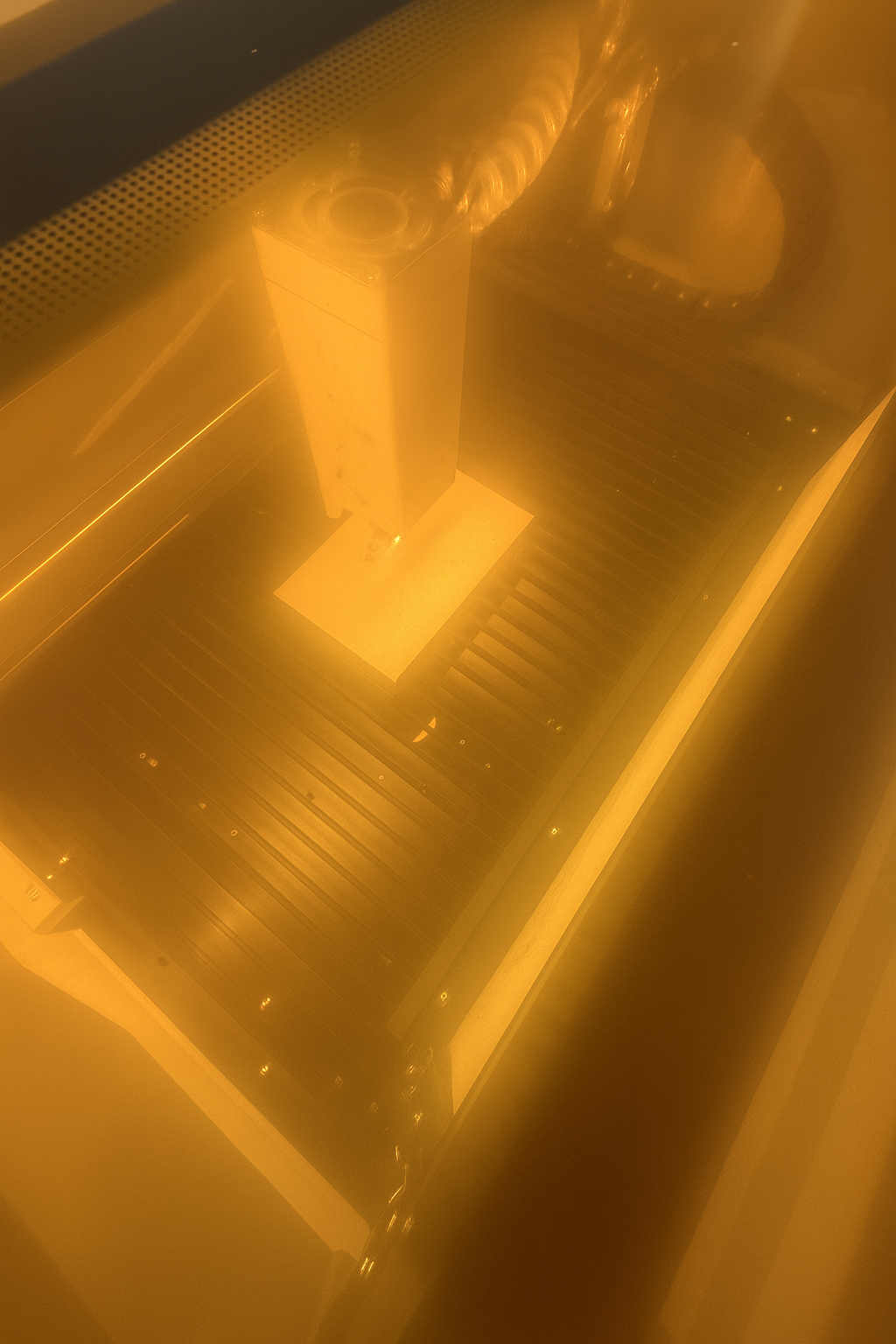 View through a yellow-tinted glass showcasing a metallic staircase and a tall rectangular object with circular openings on top.