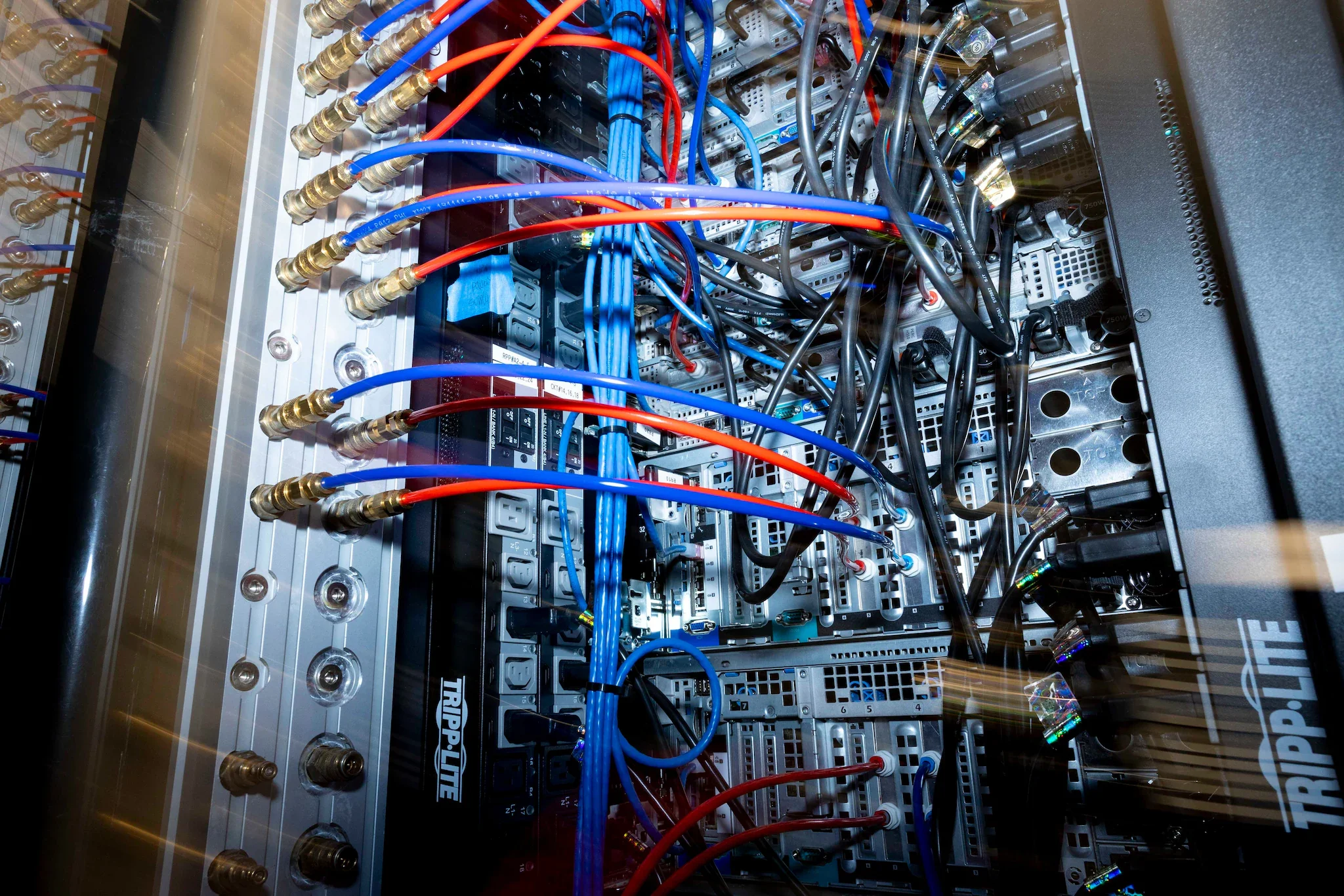 An electrical or electronic control cabinet with various interconnected wires, cables, and components. The wires are primarily blue, red, and black, connecting to circuit boards and terminals inside the cabinet.