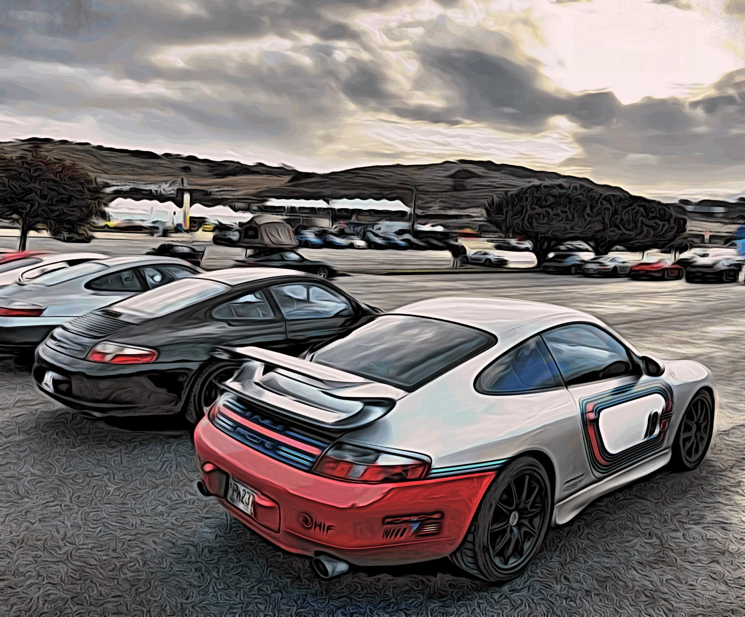 A parking lot with multiple Porsche sports cars, including a white and red Porsche with a large rear wing, during cloudy weather with a hill and trees in the background.
