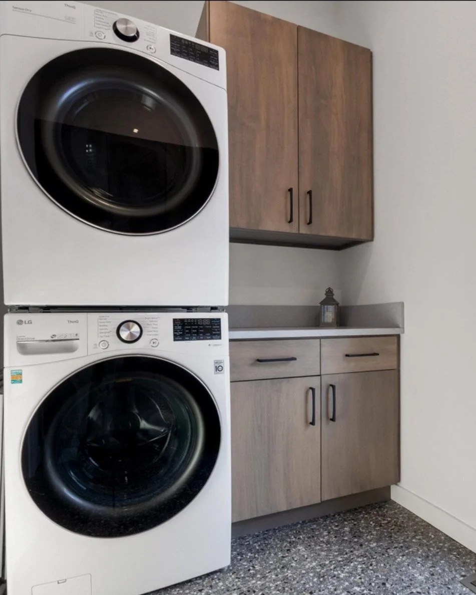 Stacked washer and dryer in a laundry room with wooden cabinets and a gray countertop.