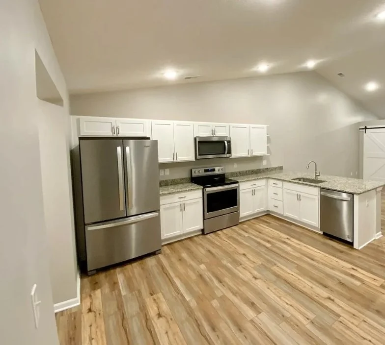 Modern kitchen with stainless steel refrigerator, stove, microwave, dishwasher, white cabinetry, granite countertops, and wood flooring.