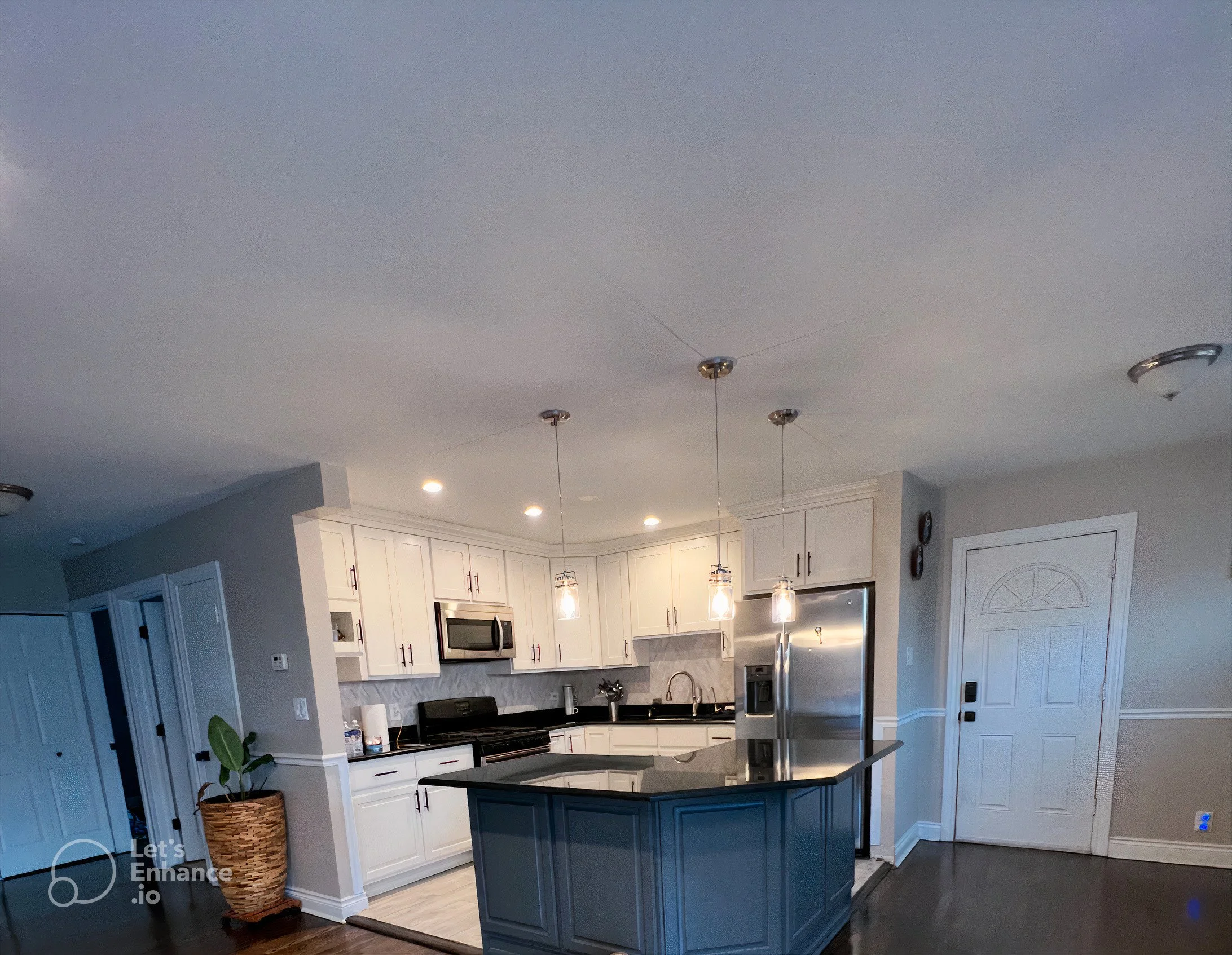 Modern kitchen with white cabinets, black countertops, a blue island, stainless steel appliances, pendant lighting, and hardwood floors.