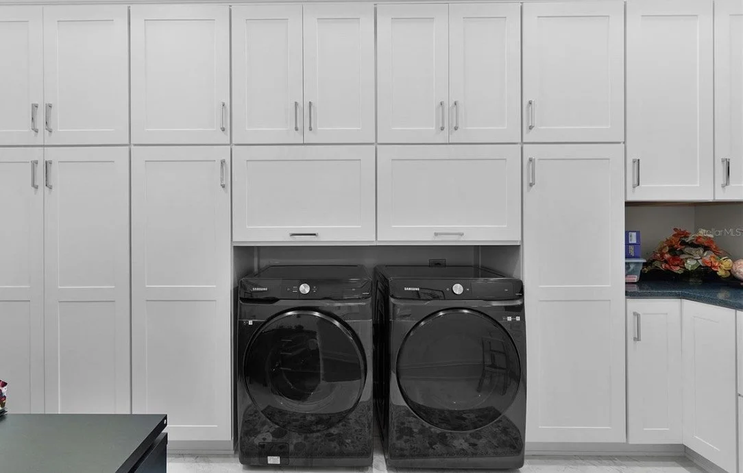 A laundry room with white cabinets and a black front-loading washer and dryer.