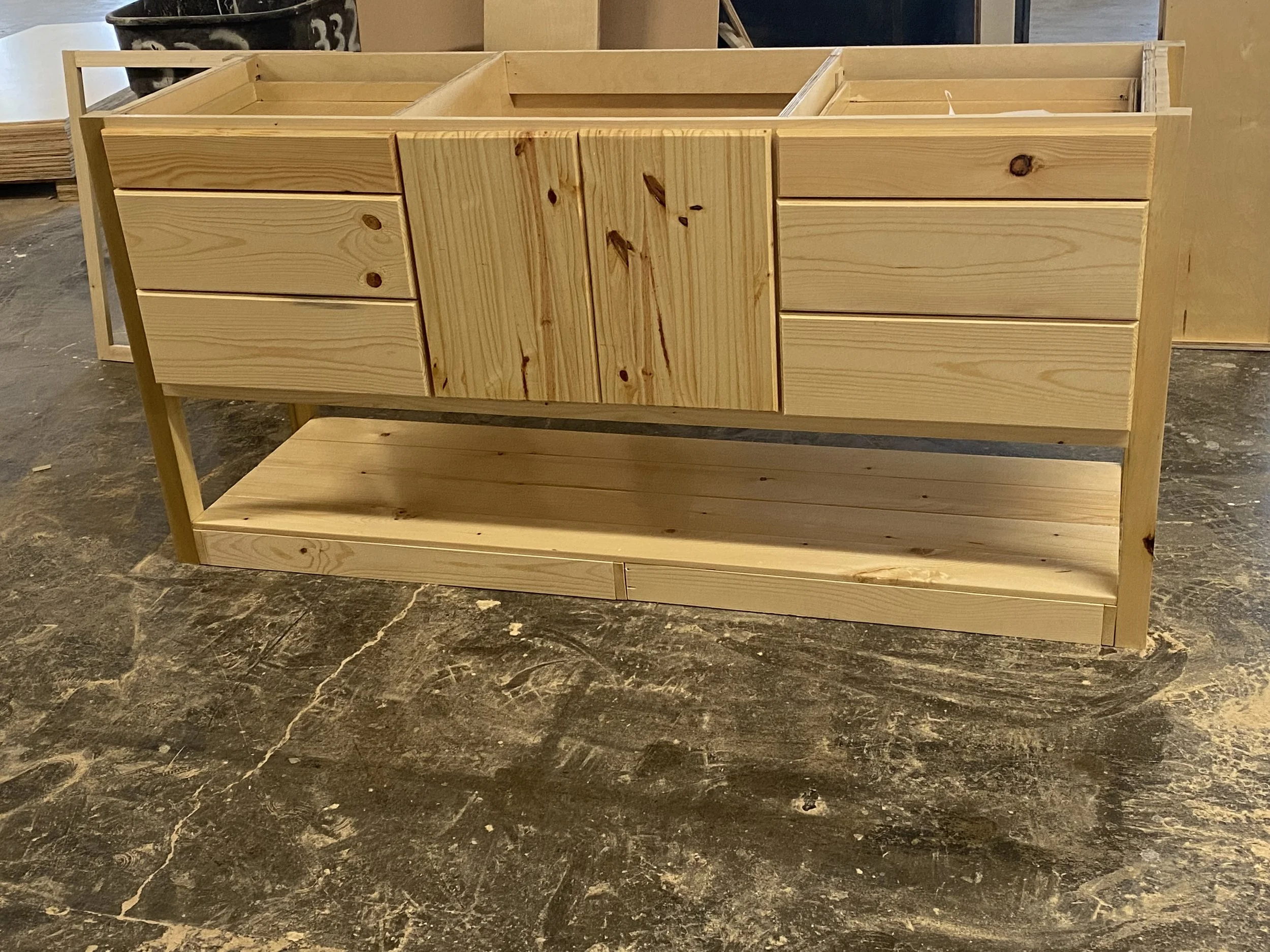  unfinished wooden cabinet with drawers and shelves in a workshop.