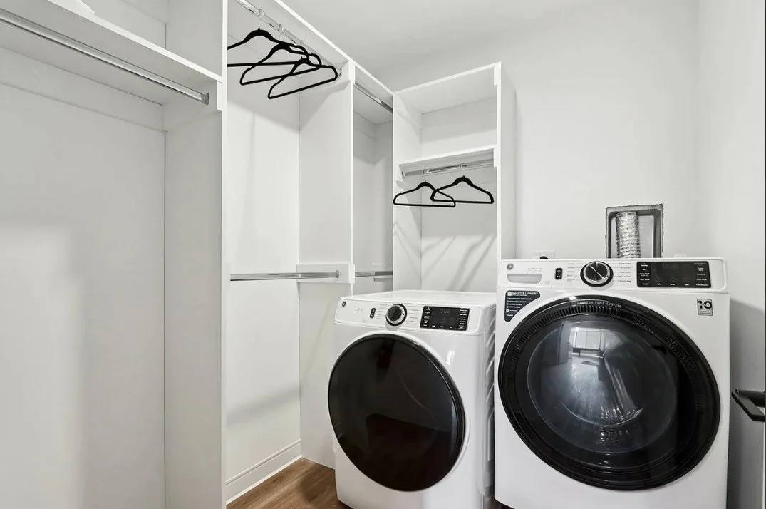 Empty walk-in closet with built-in shelves and hanging rods, next to a front-loading washer and dryer in a laundry room.