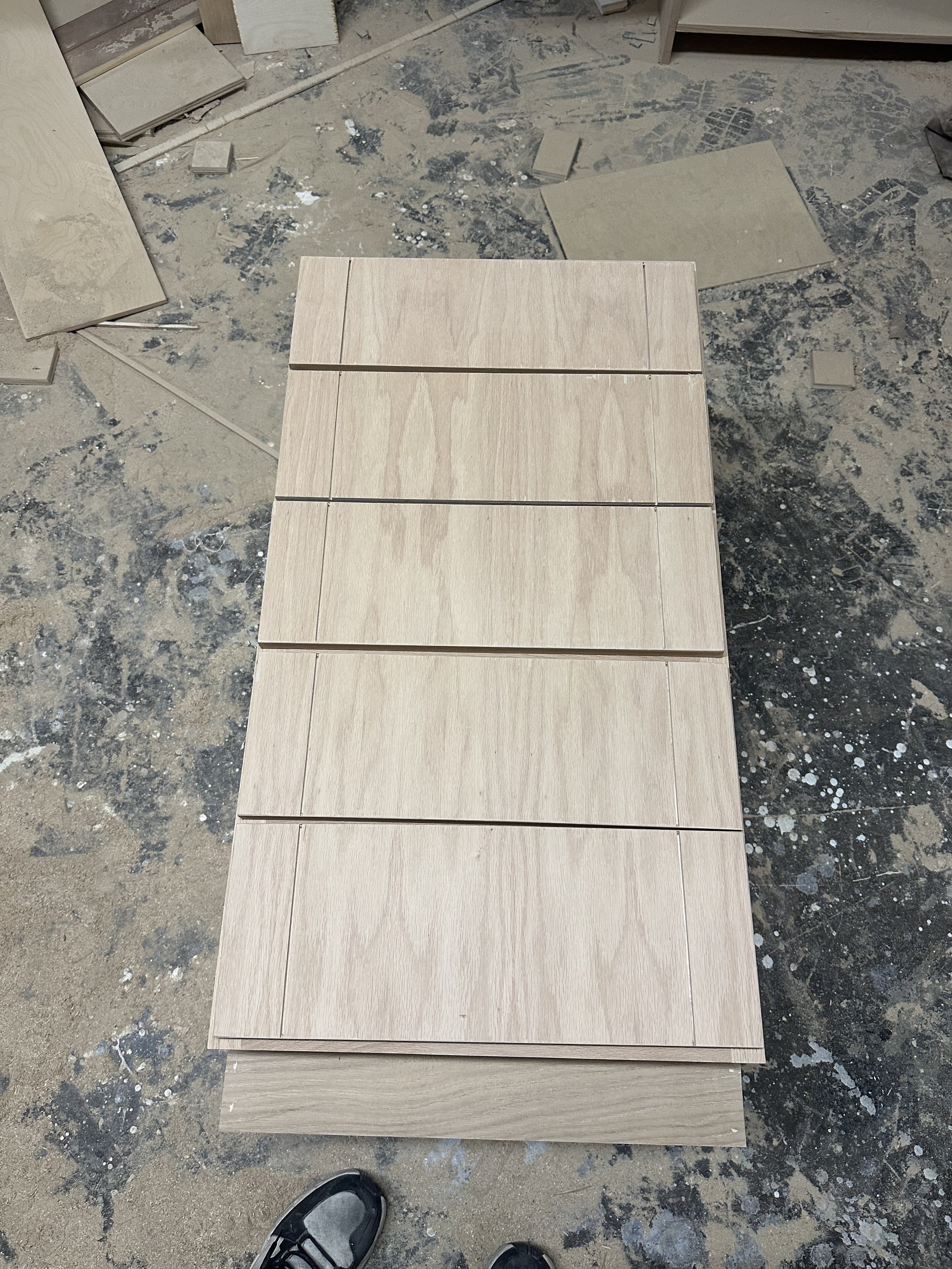 A wooden panel with five sections, placed on a worksite floor with scattered tiles and dust.