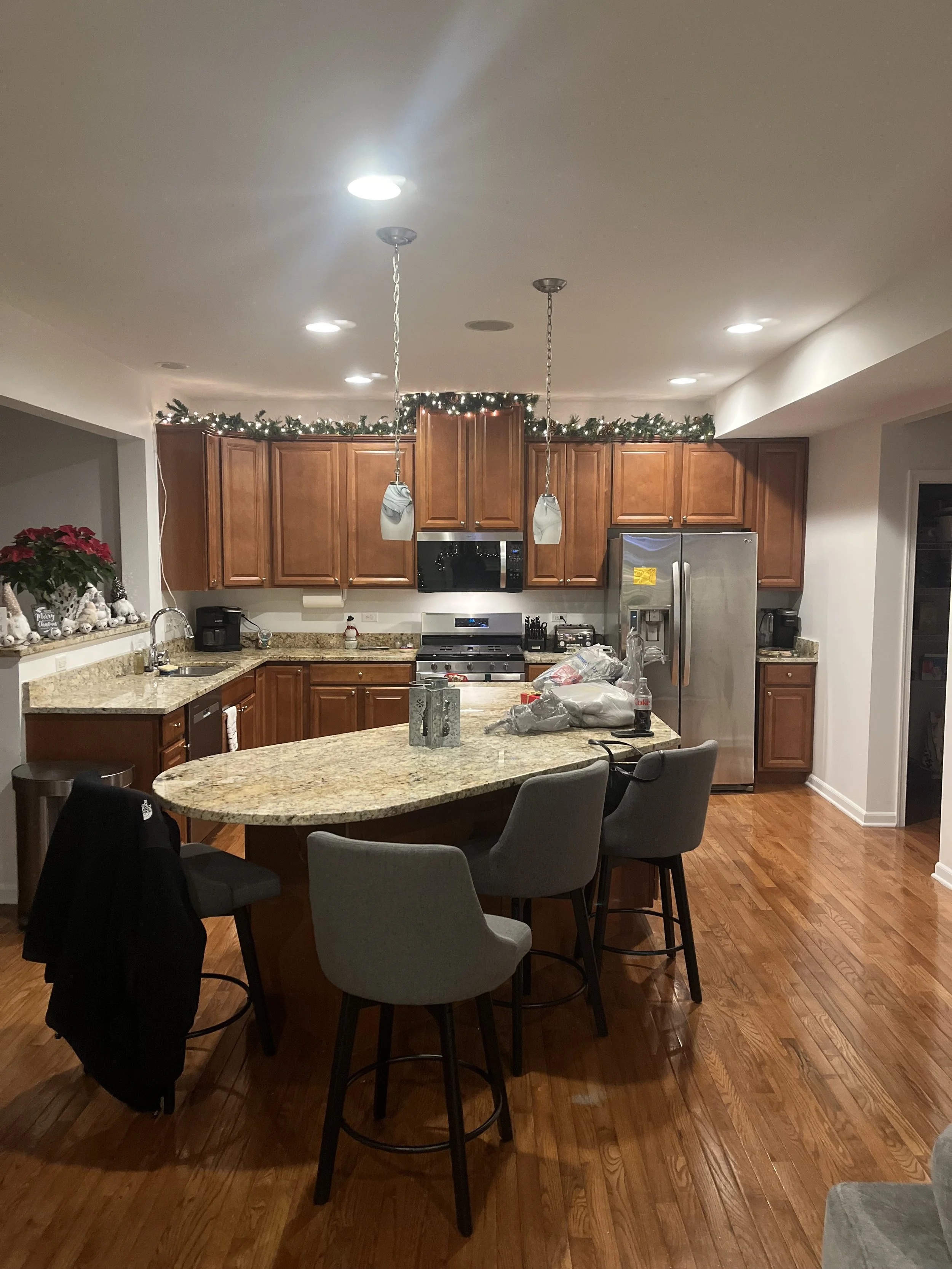 A kitchen with wooden cabinets, granite countertops, and stainless steel appliances, decorated with holiday garlands and poinsettias.