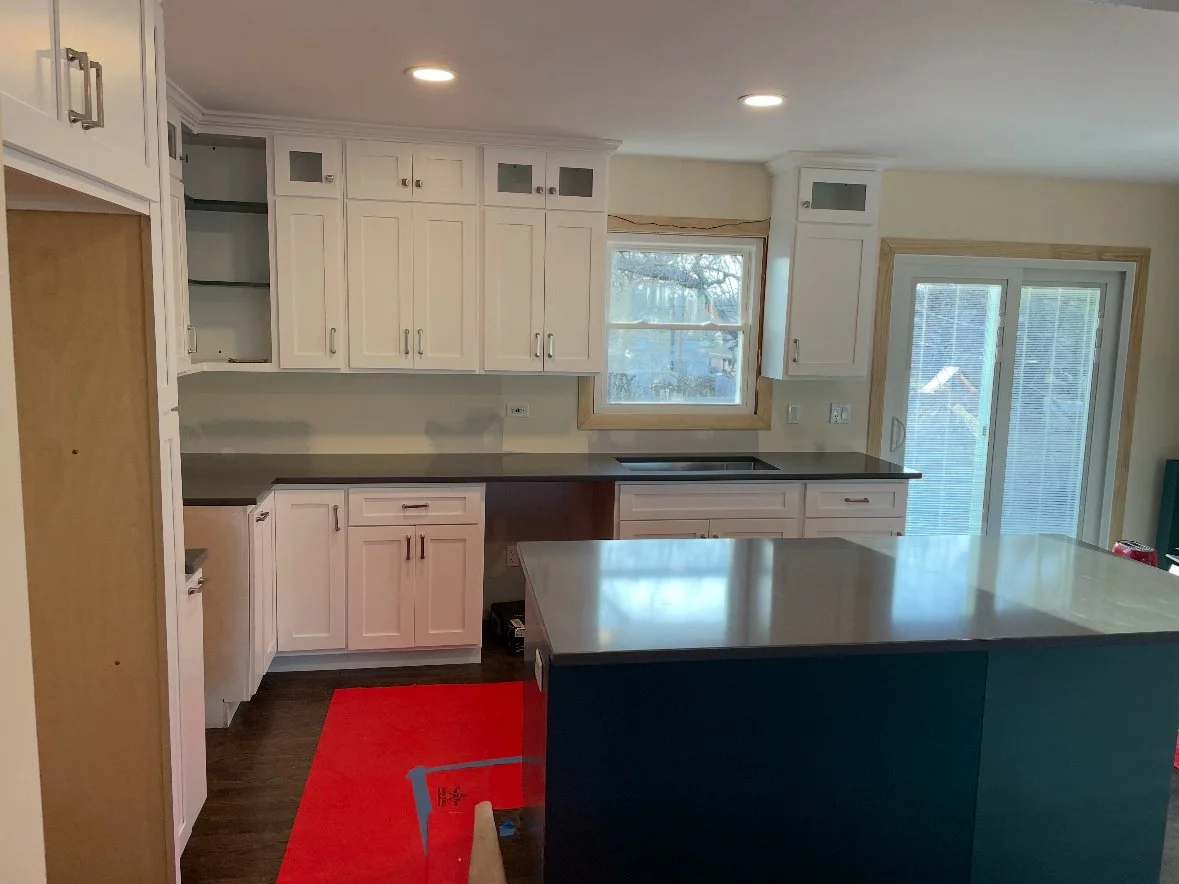 Kitchen with white cabinets, a large dark island, a window, sliding glass door, and hardwood floors.