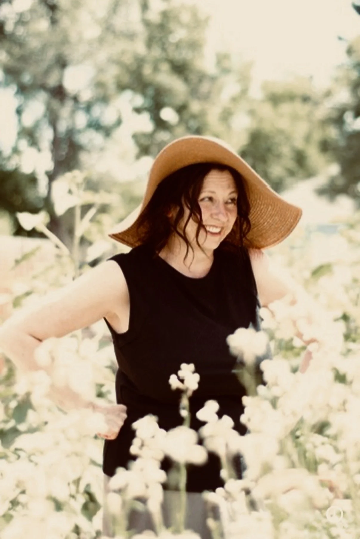 A woman smiling and wearing a large sun hat in a field of white flowers.