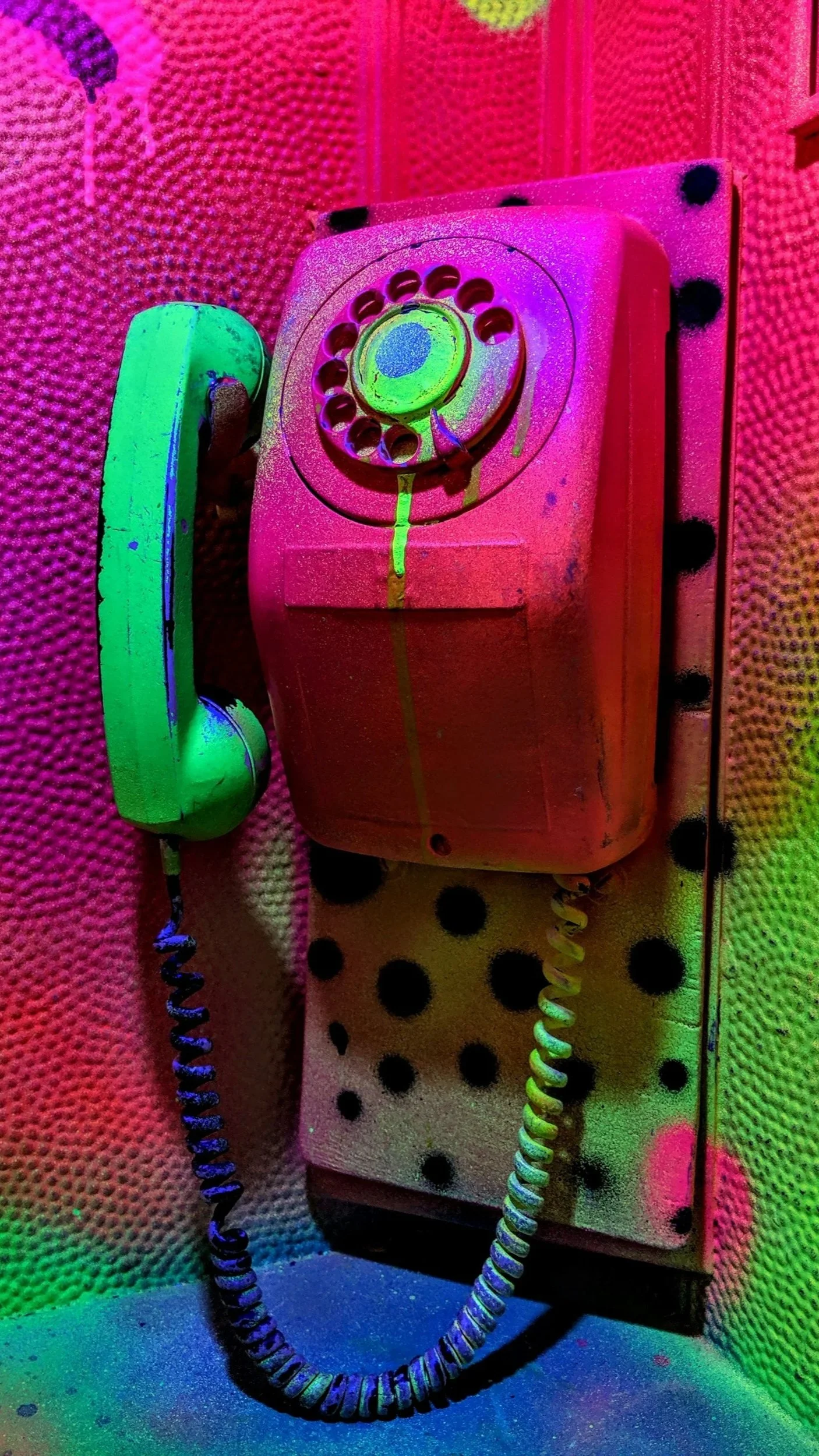 Colorful neon-lit vintage wall-mounted rotary telephone with a coiled cord, depicted in vibrant pink, green, and yellow hues.