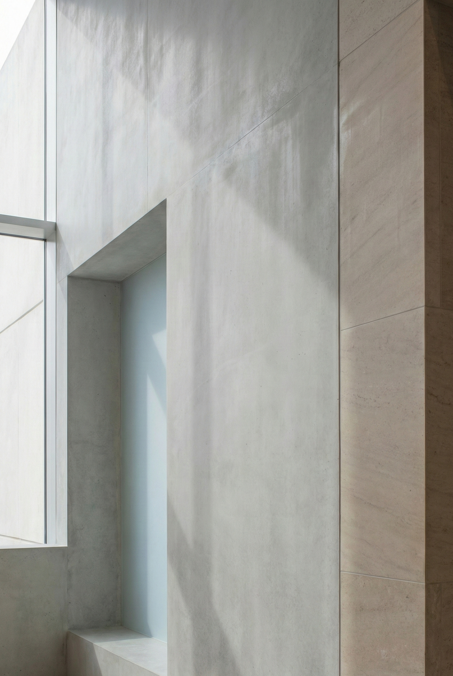 Interior of a modern building with light-colored concrete walls, a window, and shadows cast by a plant or object.