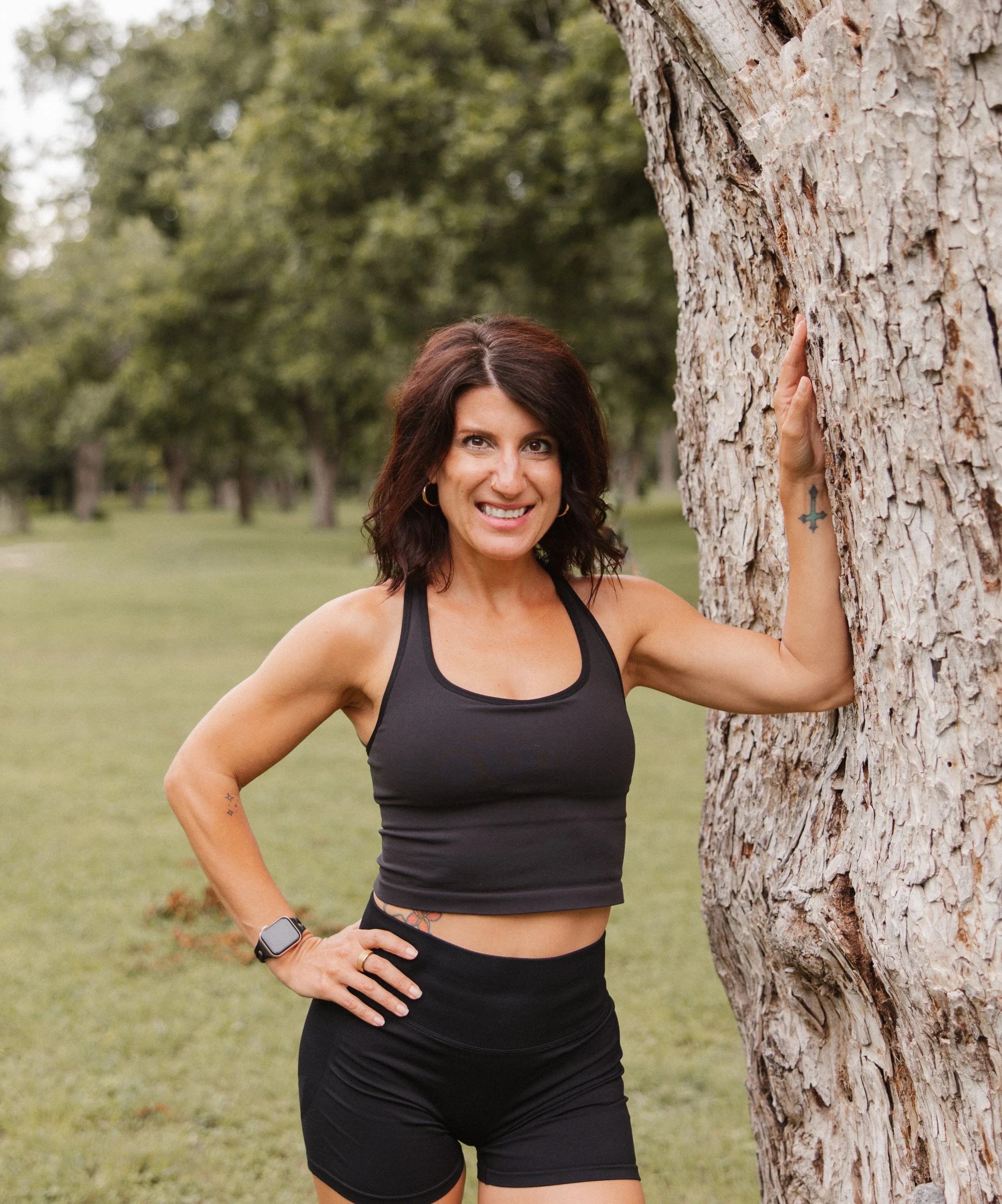 A woman with black hair, wearing a black sleeveless top and leopard-print pants, standing in front of a pink background.