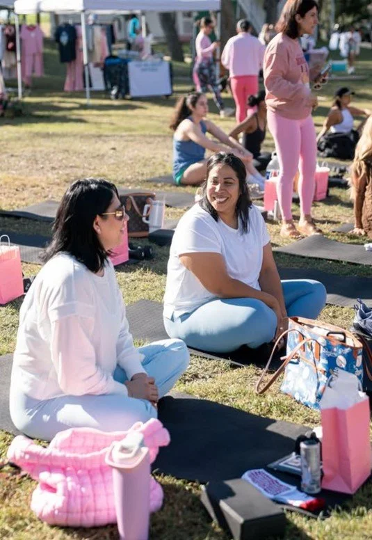 People participating in an outdoor yoga or meditation event, sitting on yoga mats and engaging in conversations on a grassy area.