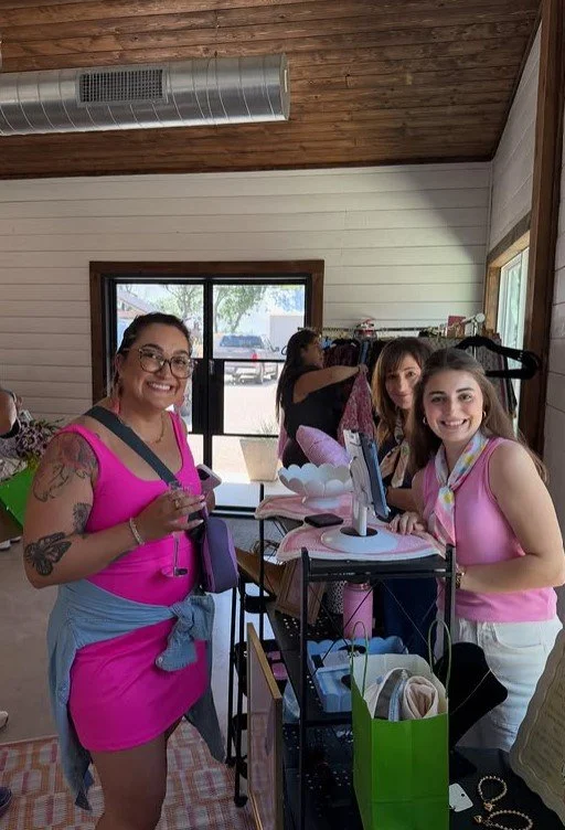 Group of women shopping indoors, smiling, with clothing and accessories displayed.