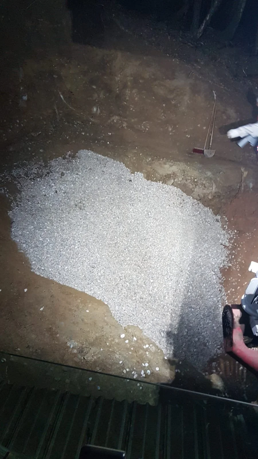 Boden mit einer Schicht aus kleinen weißen Kieselsteinen, umgeben von Erde, mit Werkzeugen im Hintergrund.