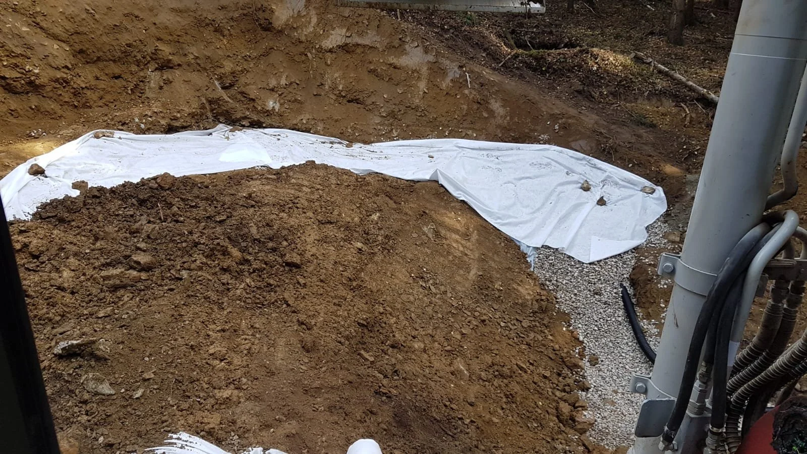 Ausschnitt einer Baustelle mit Erde, weißen Abdeckungen und einem Kabelstrang.