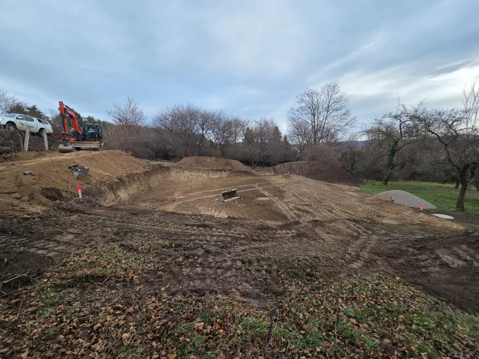 Baustelle im Freien mit Bagger, Erde LKWs und Bäume im Hintergrund.