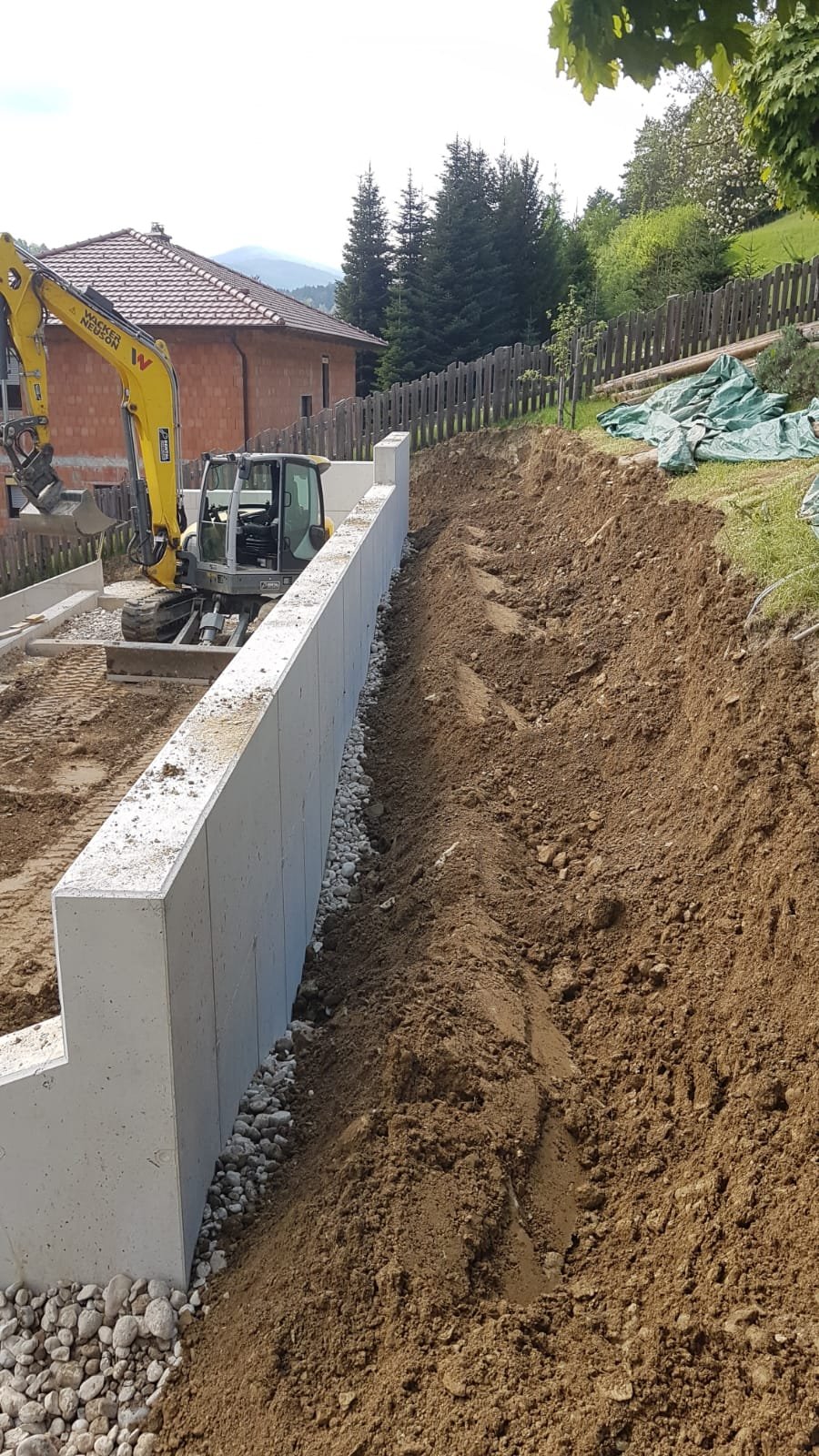 	
Baustelle mit Bagger, der auf einer geneigten Fläche Erde bewegt, und weißen Bauwänden.