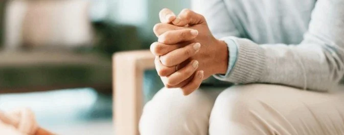 Person sitting with hands clasped together on lap