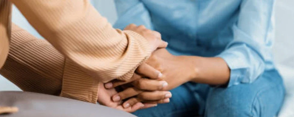 Two people holding hands in a supportive gesture, one hand over the other.