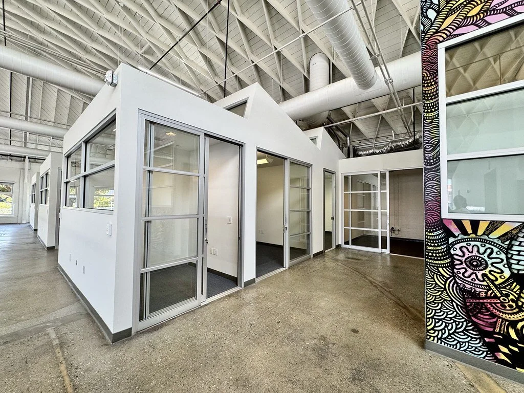 Modern office space with white partitioned rooms, glass doors, and a partial colorful mural on the right side.