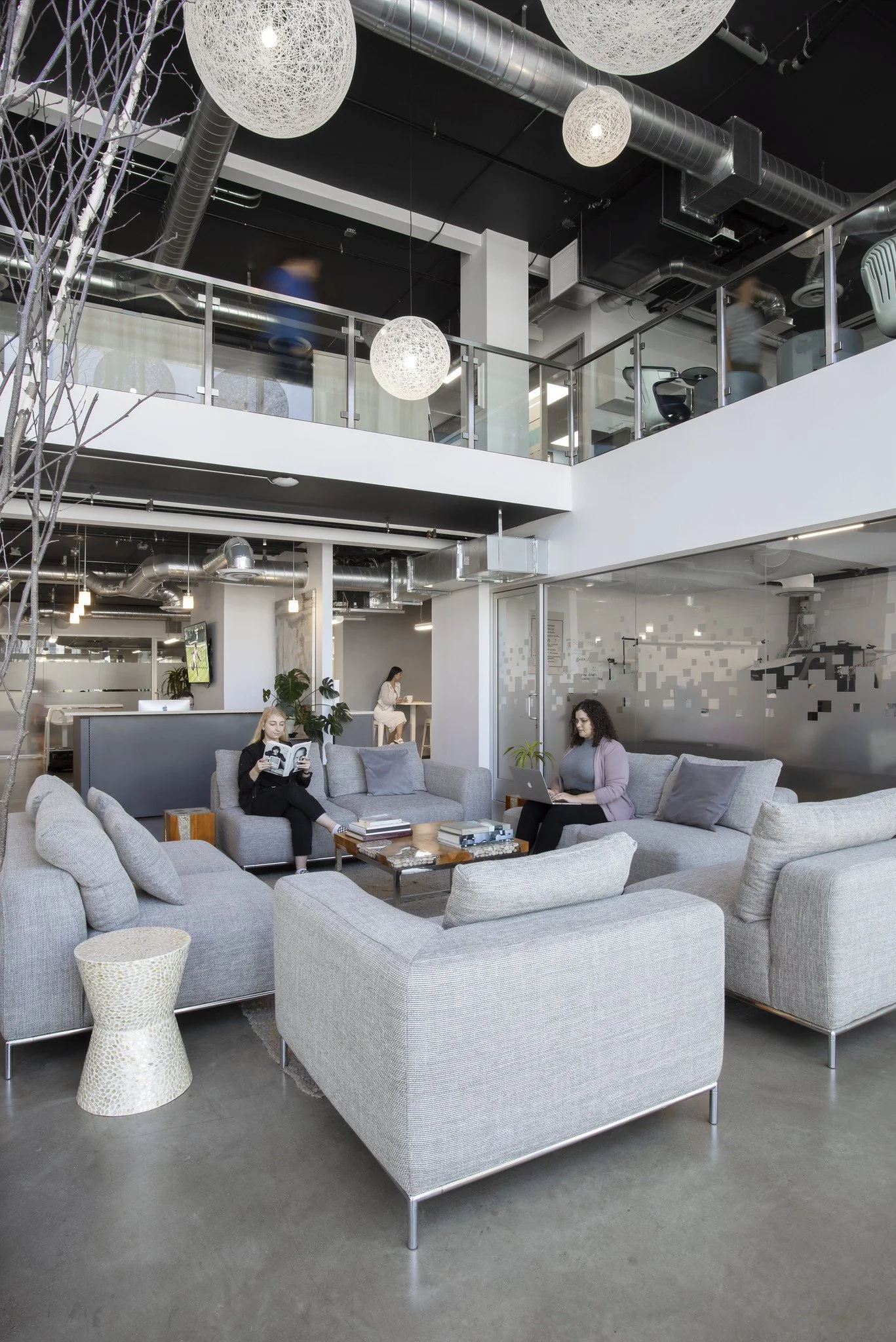Modern office lobby with gray sofas and people working on laptops and reading magazines