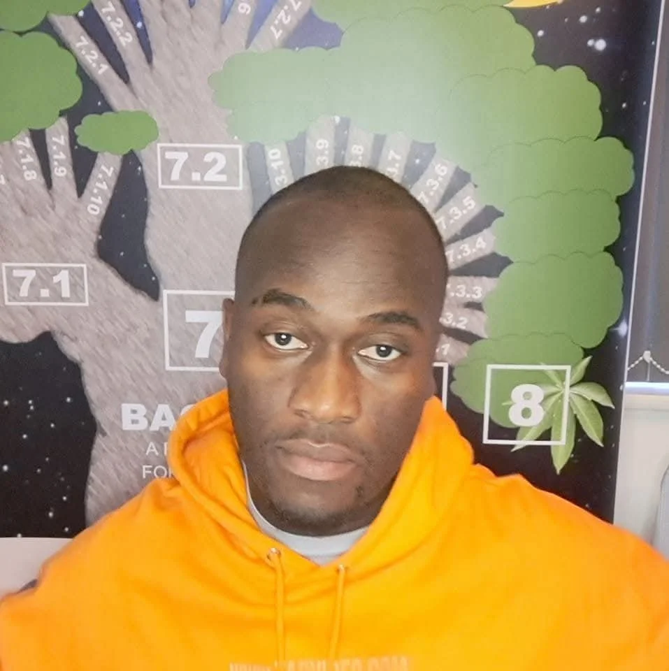 A man in an orange hoodie taking a selfie in front of a star-themed quiz wall with numbered sections and green cloud-shaped cutouts.