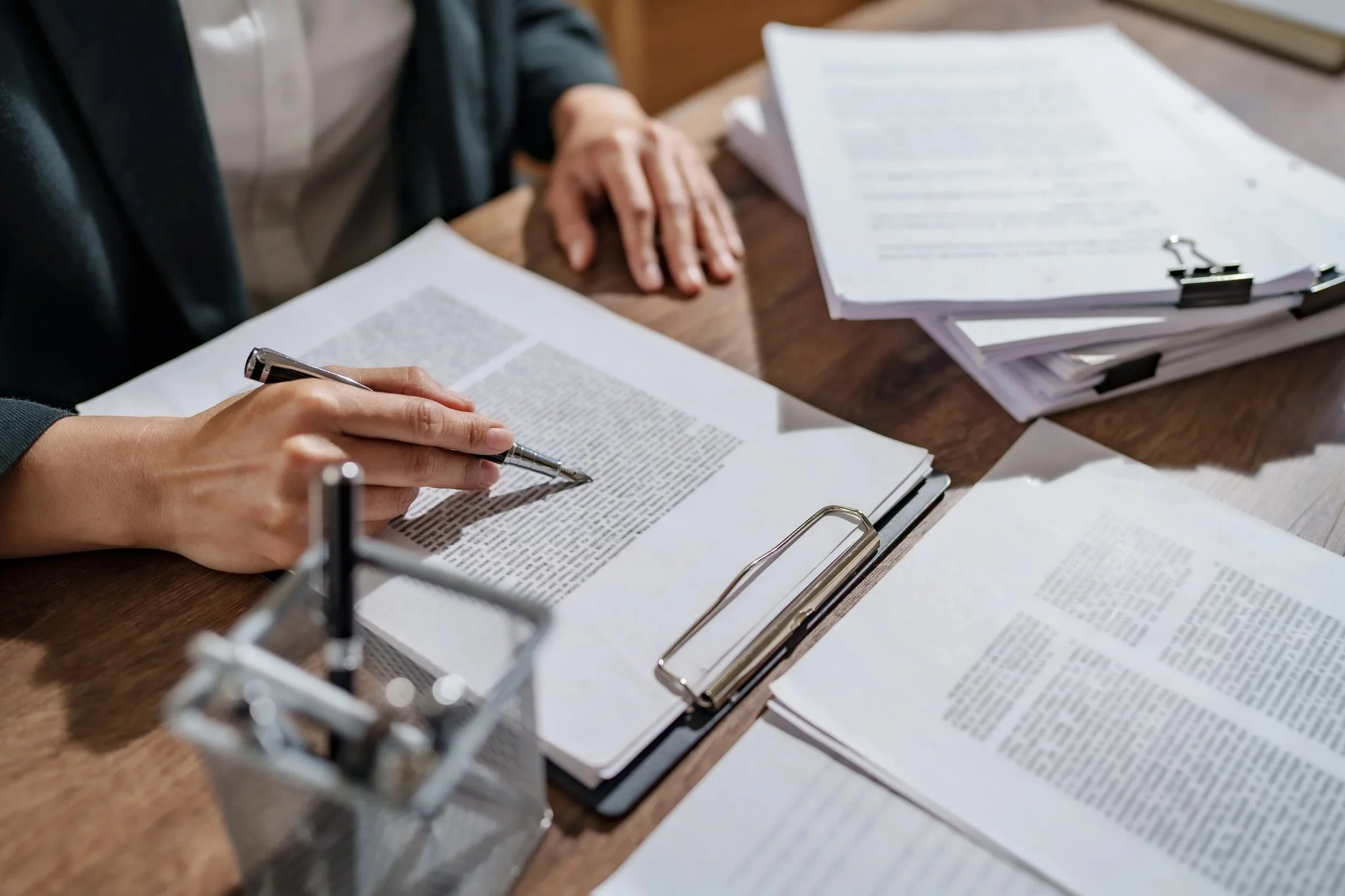 Two people reviewing legal documents at a desk with multiple stacks of papers, pens, and binder clips.