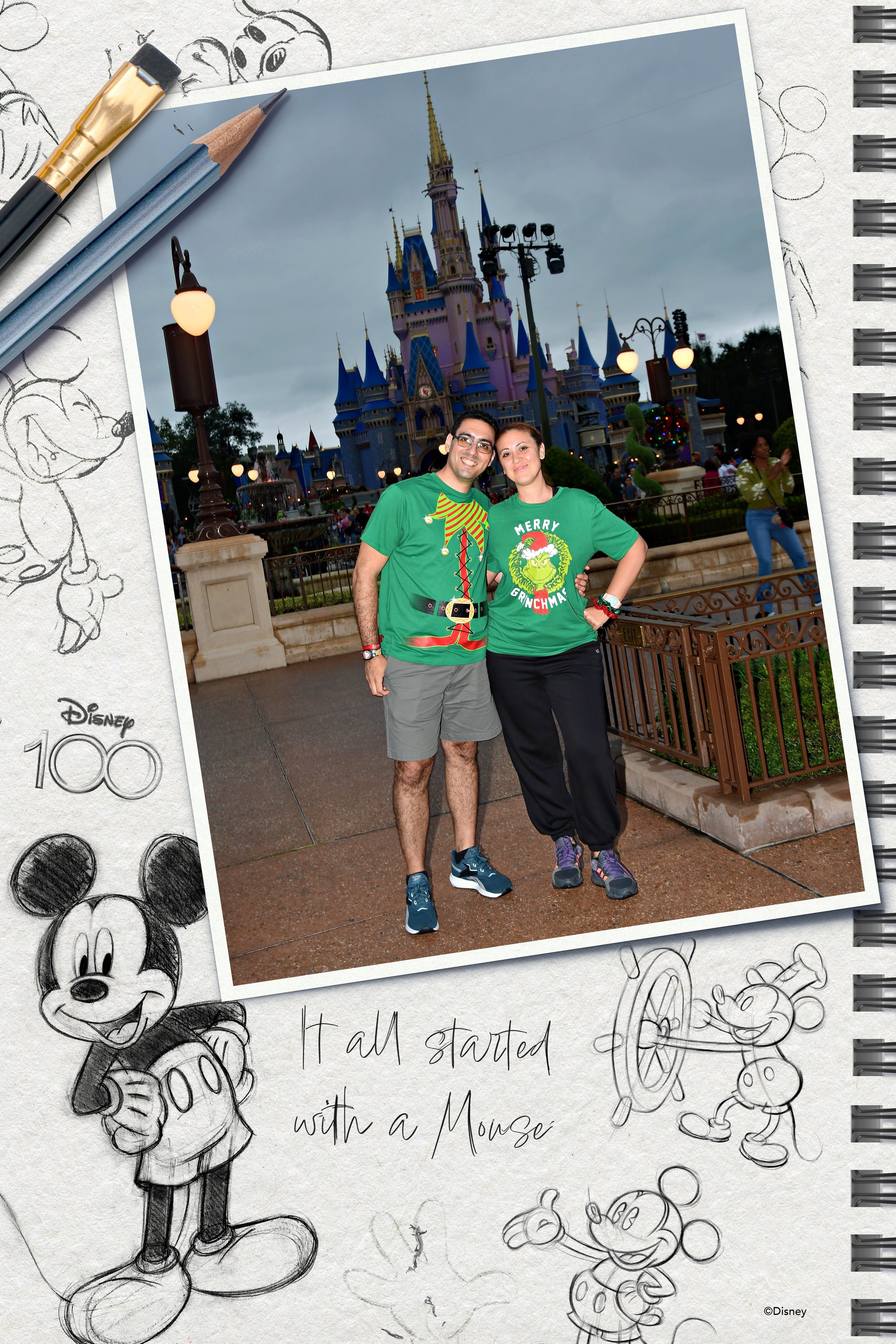 Una pareja sonriendo frente al Castillo de Disney en un parque temático, con cielo nublado y gente en el fondo, ambos llevan camisetas verdes navideñas.