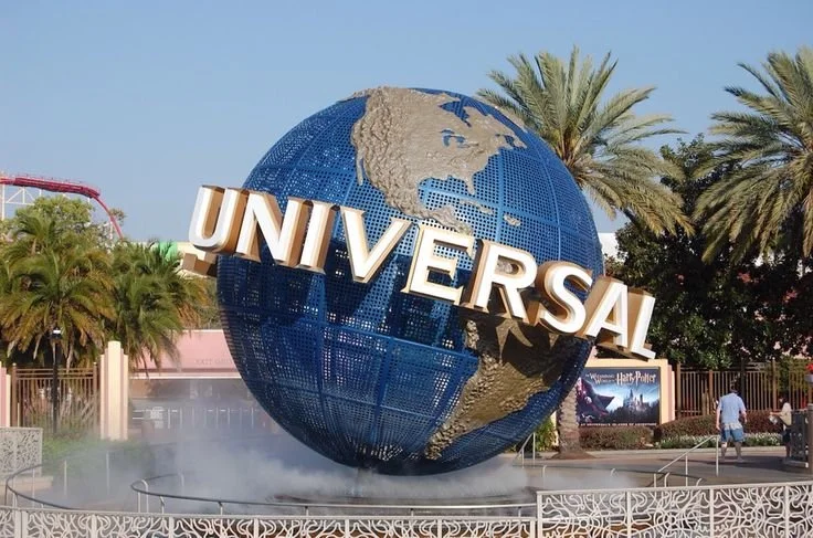 Globo terráqueo de The Universal Studios con la palabra 'Universal' en letras grandes, rodeado de palmeras y personas.
