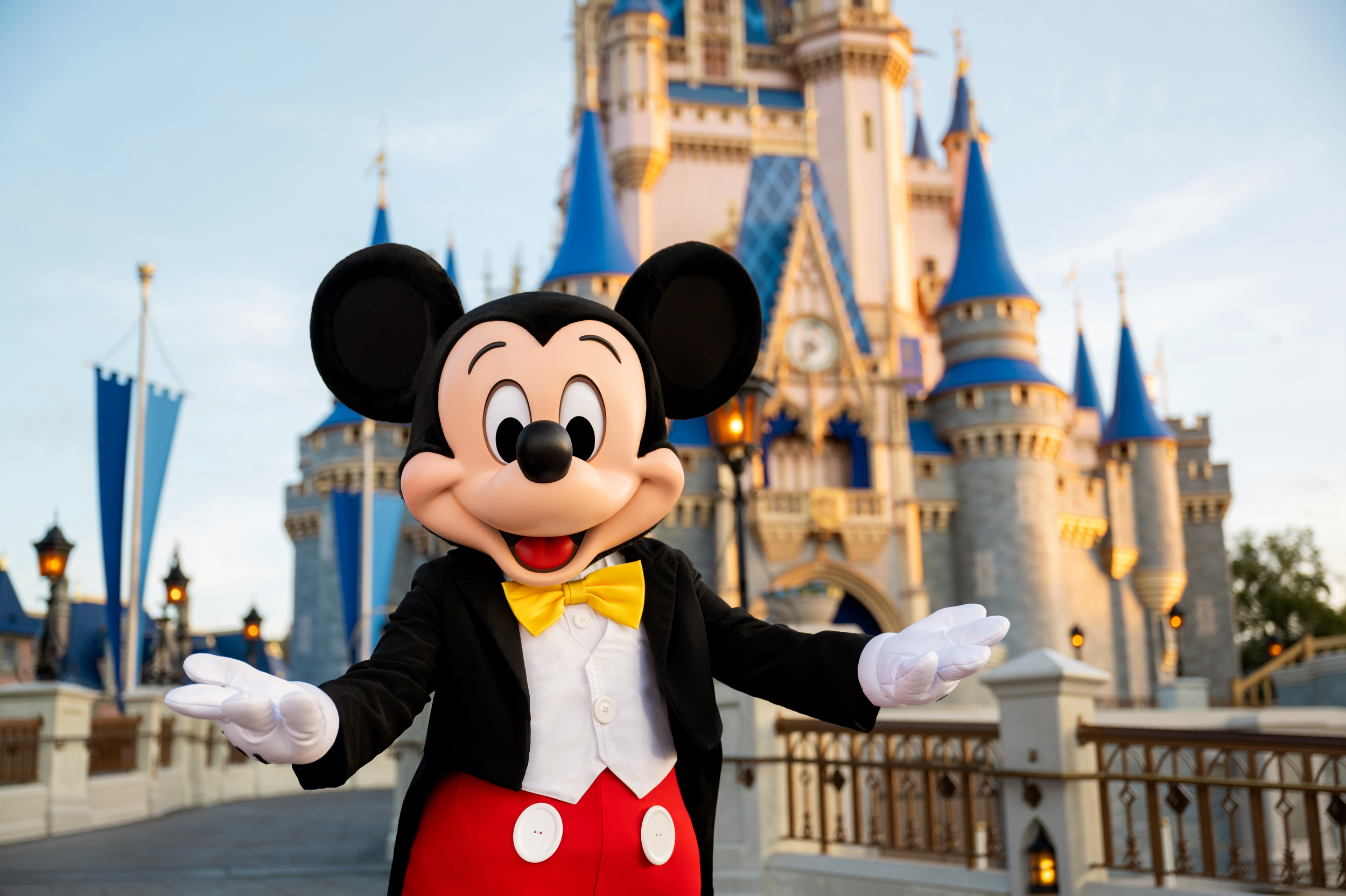 Mickey Mouse disfrazado de mayordomo en el castillo de Disney con fondo de cielo azul y nubes