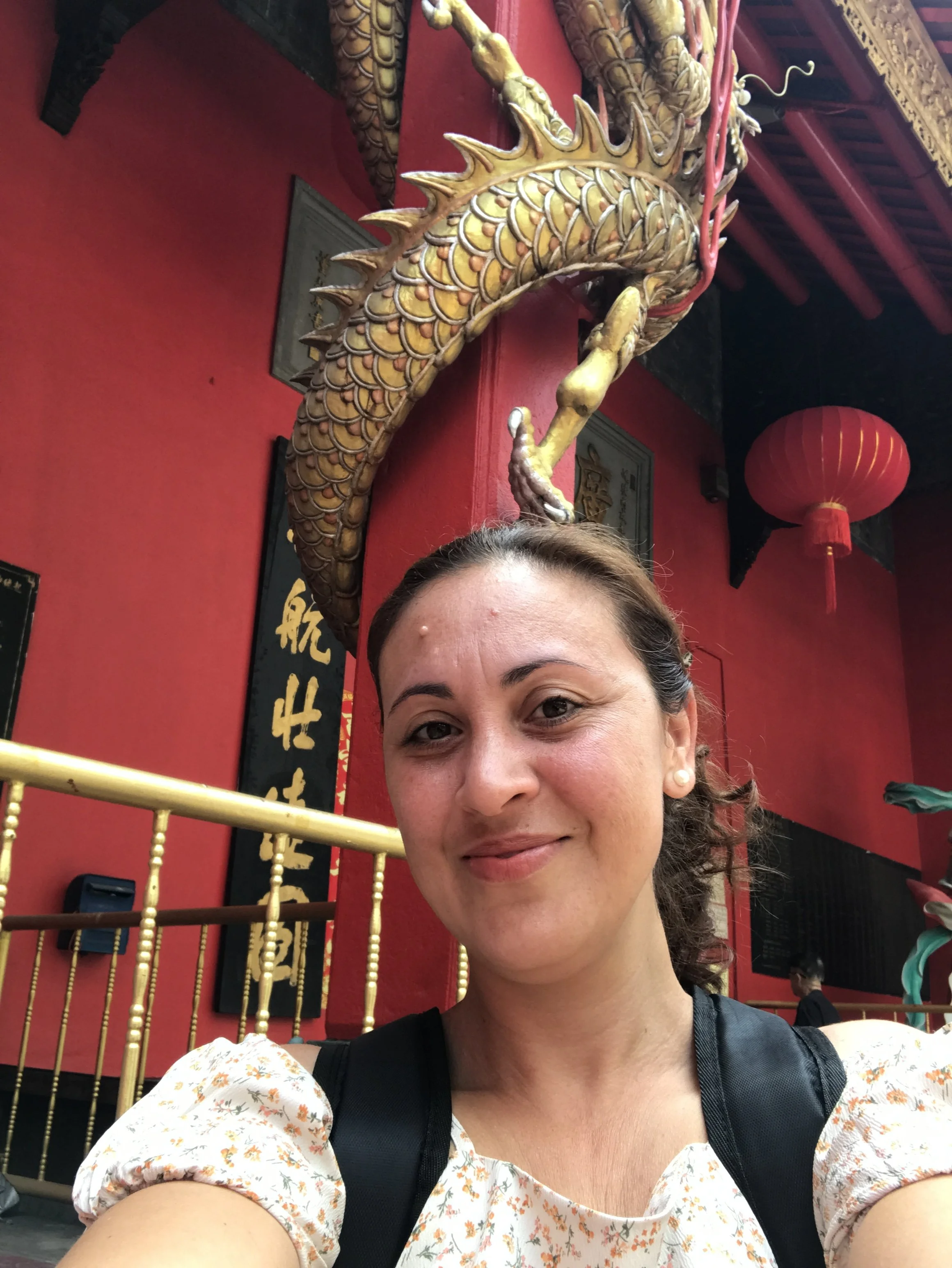 Retrato de una mujer en primer plano en un lugar decorado con temática oriental, con un dragón dorado en el fondo y lámparas de papel rojas.