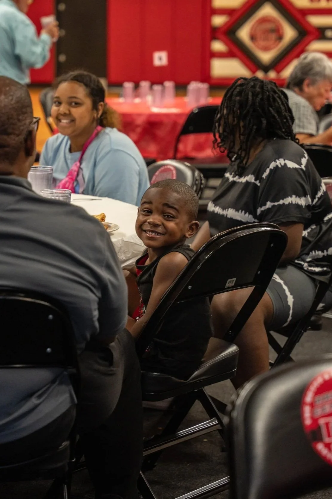 A young boy smiling at a restaurant table surrounded by adults.