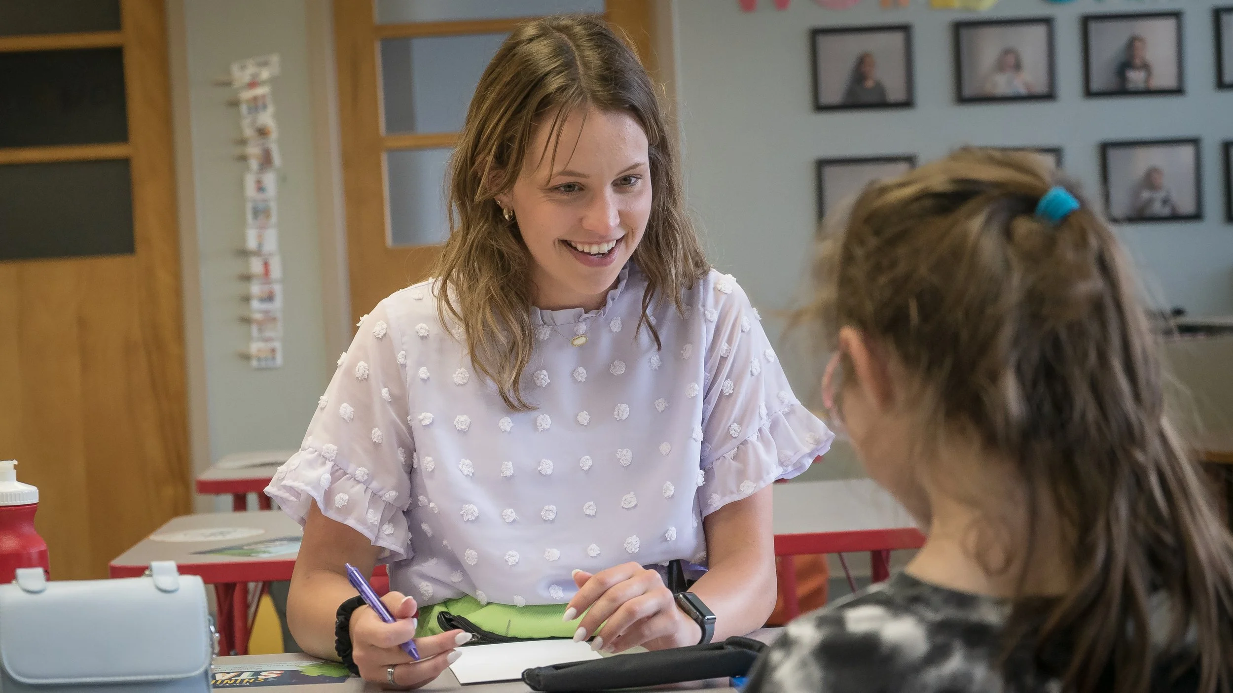 A woman smiling and talking to a girl in a classroom setting.