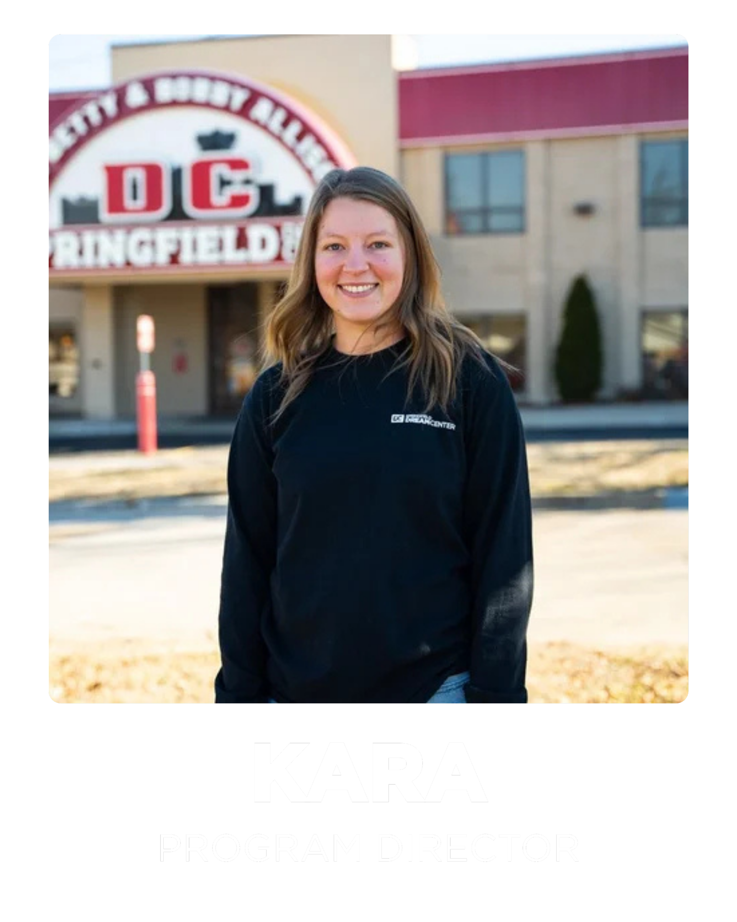 A woman with shoulder-length brown hair smiling in front of a building with a red and white sign that reads "DC Springfield." She is wearing a black sweatshirt with a logo on the chest. The text overlay at the bottom reads "Kara, Program Director."