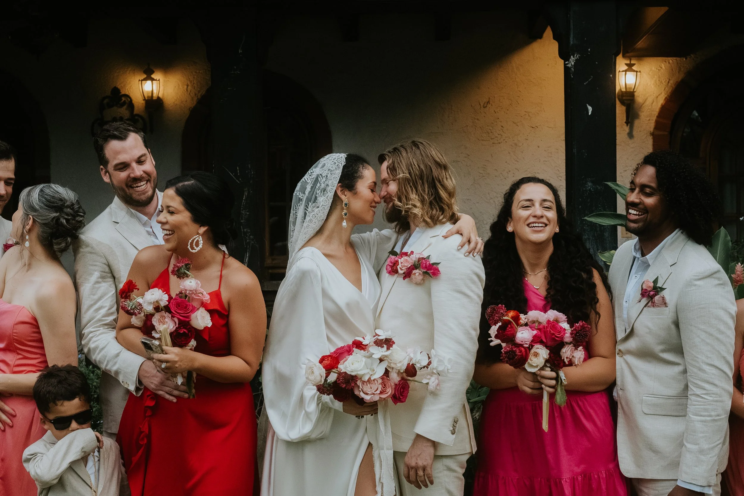 A group of people dressed in formal attire, gathered outdoors, with some holding bouquets of flowers, celebrating at a wedding or special event.