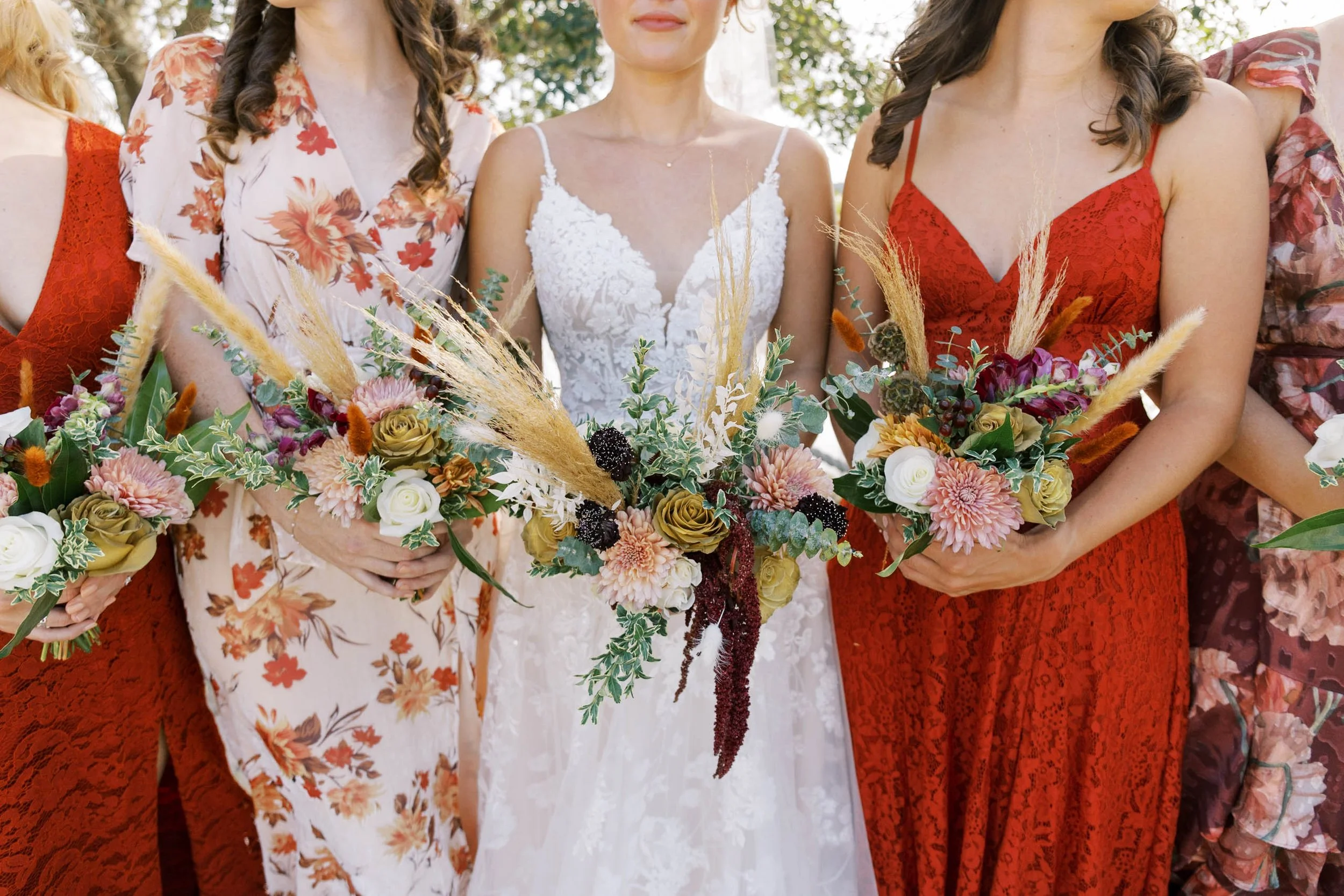 Close-up of women holding floral bouquets at a wedding, wearing colorful dresses with floral patterns.