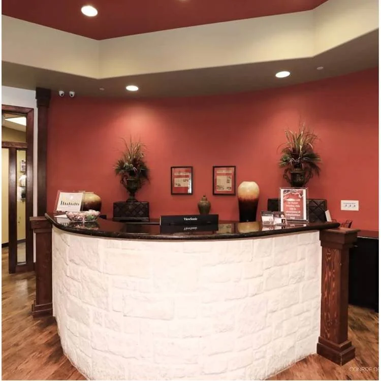 Reception desk with decorative vases and plants against a red wall.