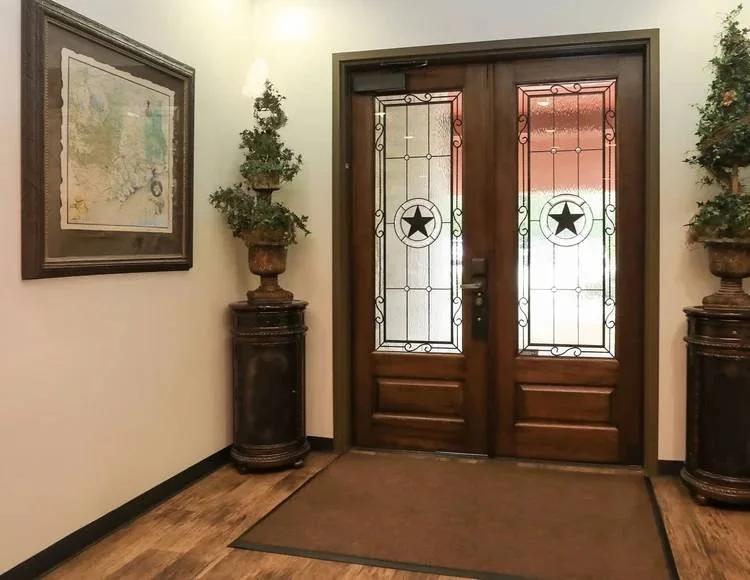 Entryway with wooden double doors featuring stained glass and star designs, flanked by potted plants on carved stands, and a framed map on the wall.