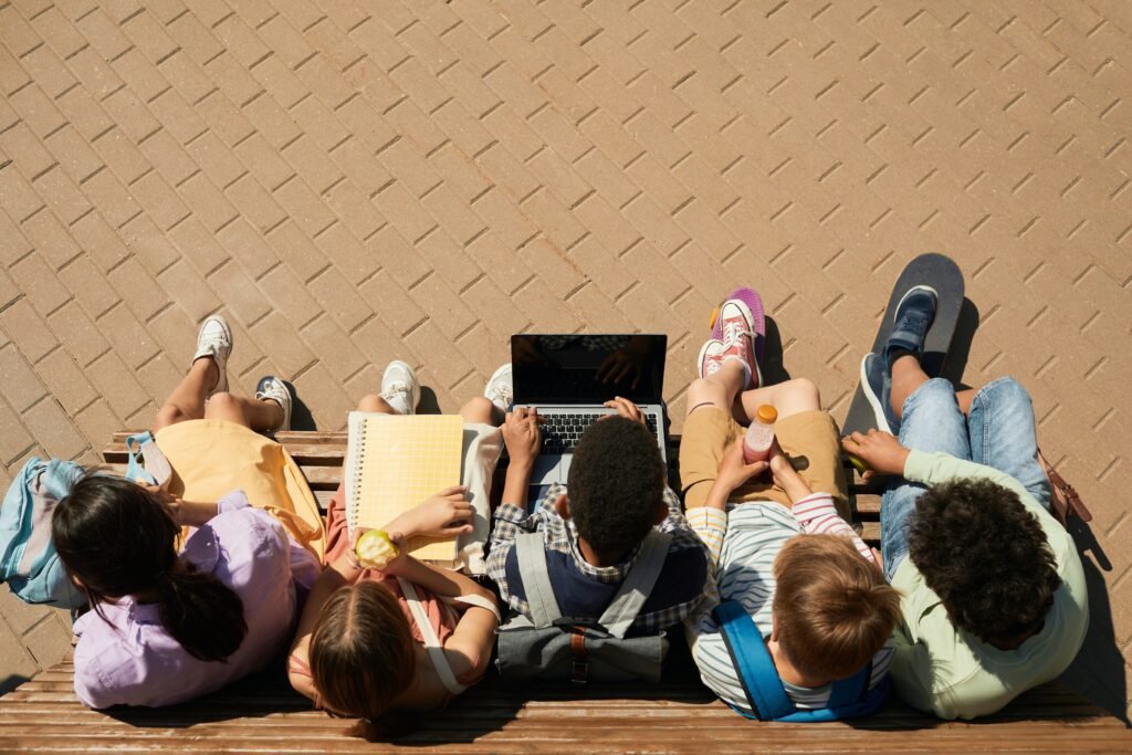 Aerial view of students studying on a bench with laptops and notebooks for the blog post Education Systems Around the World: A Look at 4 Top School Systems
