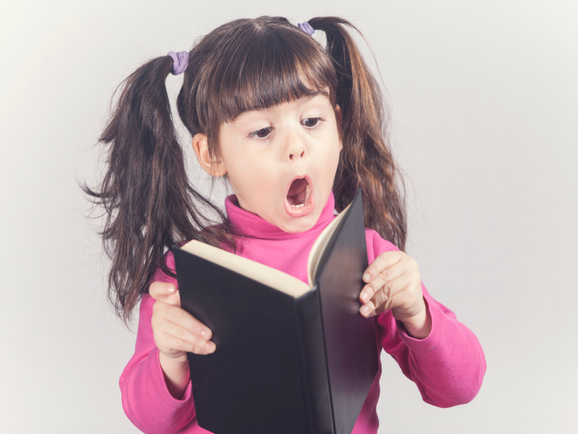Child reading a book with a surprised face