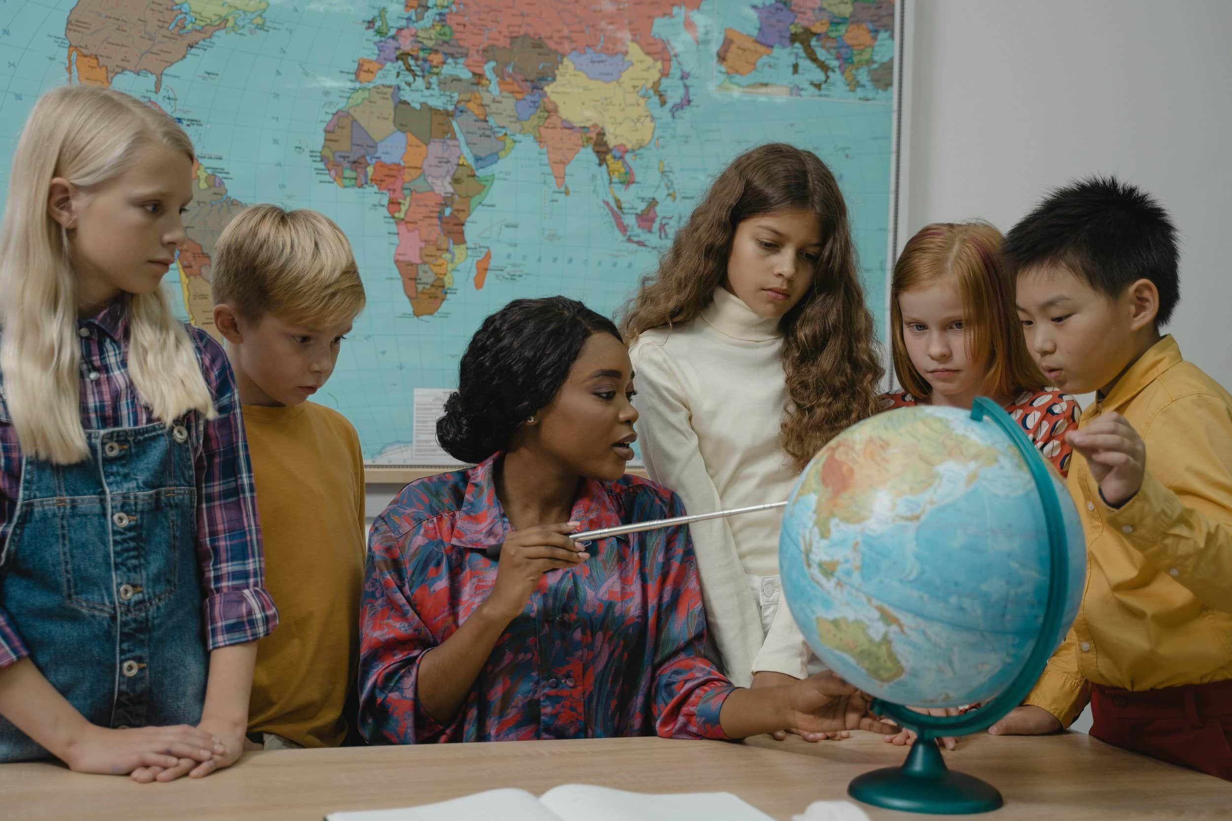 Image of teacher pointing at a globe surrounded by five students.