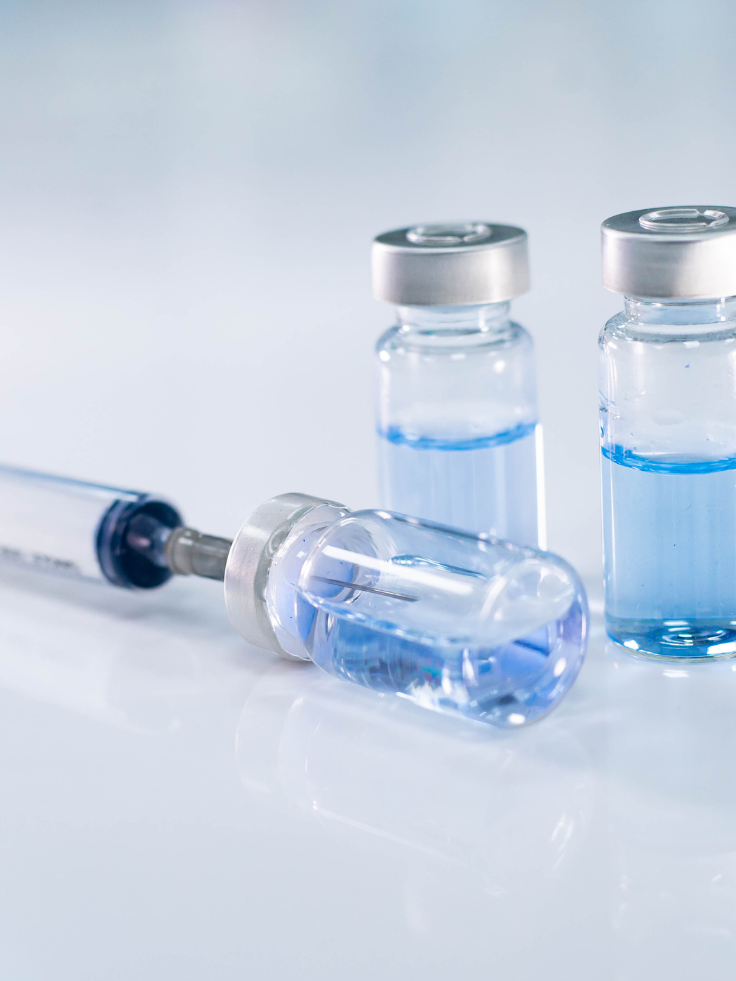 Two small glass vials filled with clear liquid and a syringe with a needle, placed on a white surface.