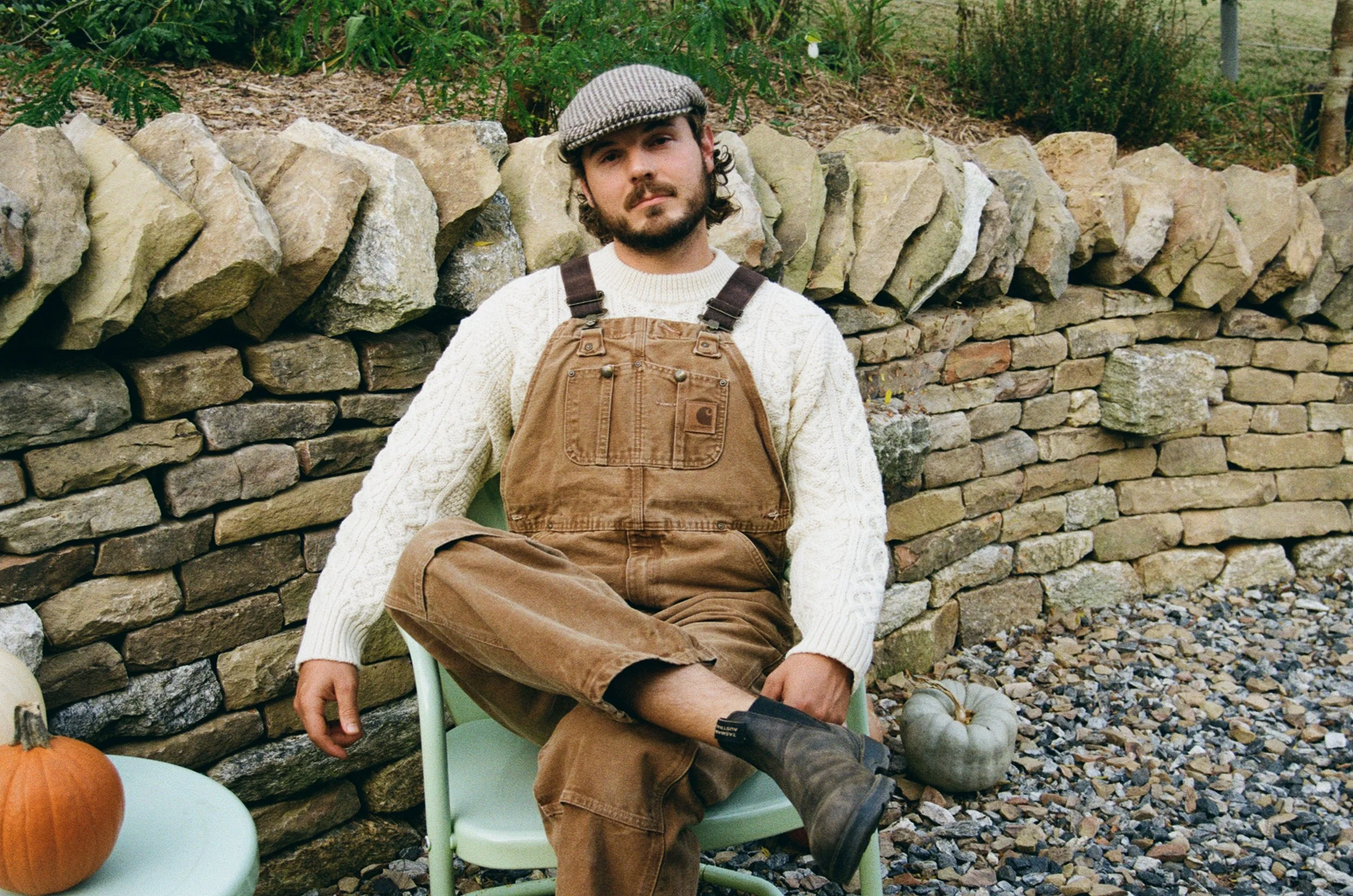 a man in overalls sitting in front of a dry stone wall