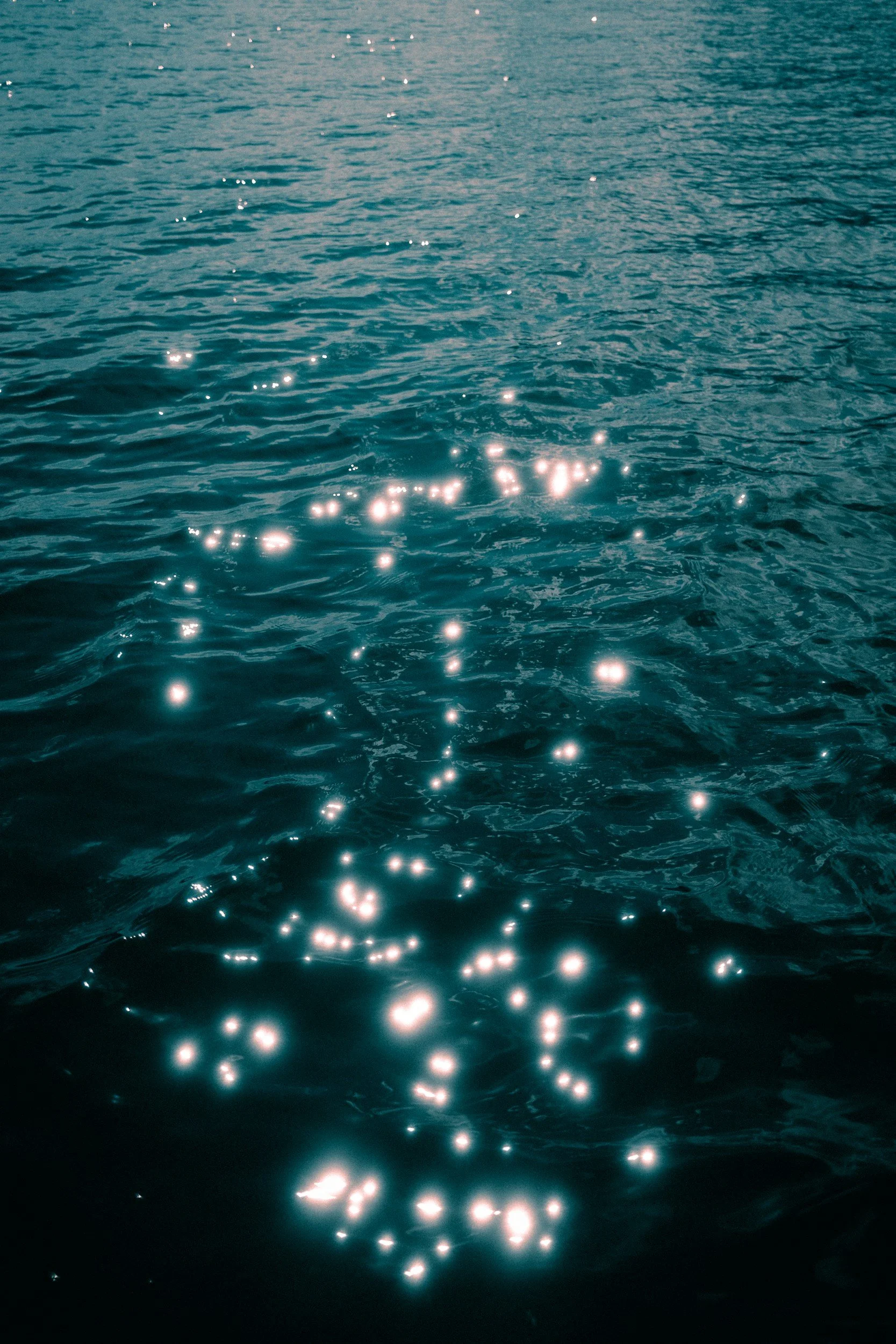 Sunlight reflecting off the surface of a body of water, creating bright, sparkling spots on the rippling water.